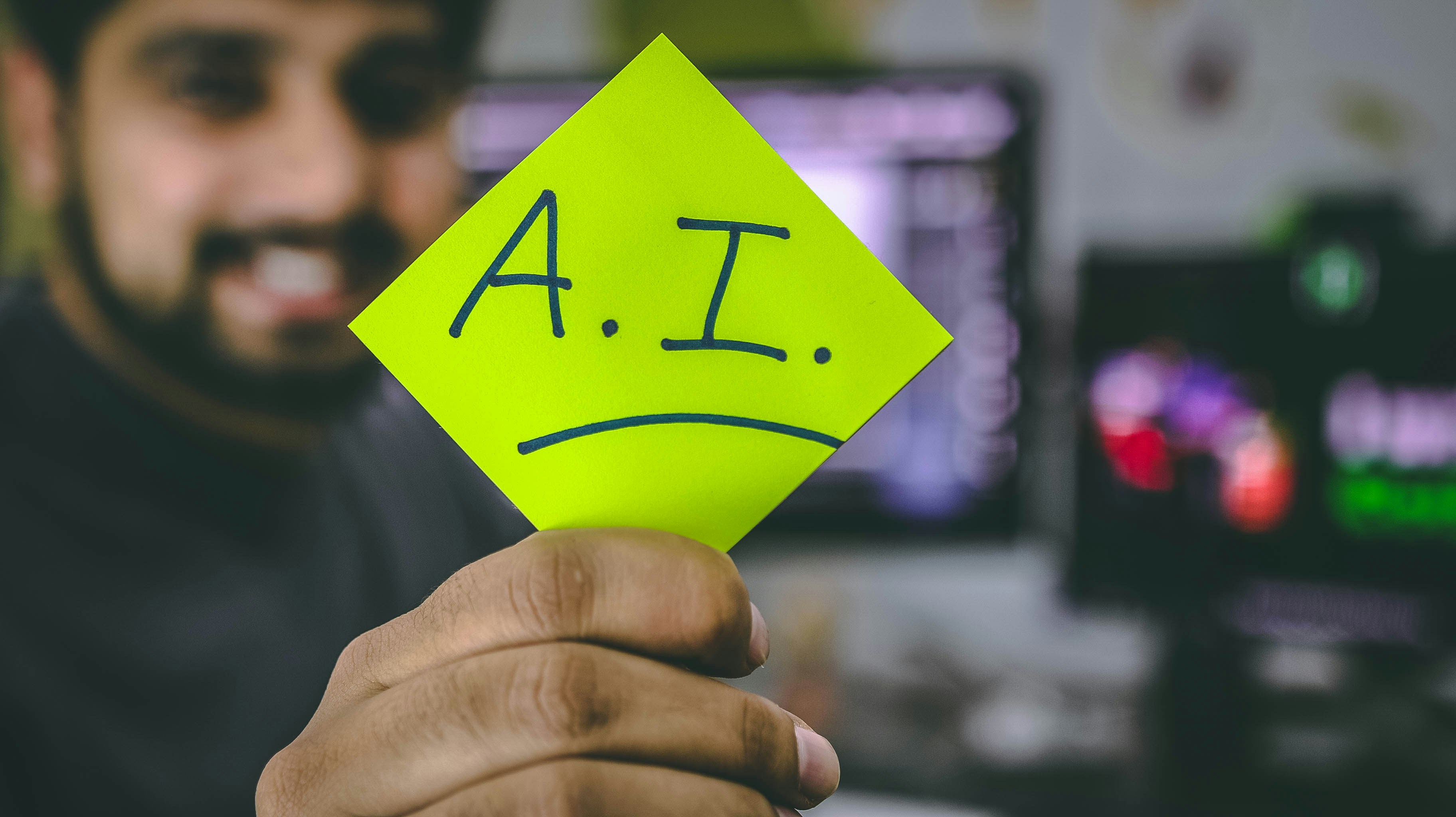 A person holding a sticky note with "AI skills" written on it, with a blurred background of computer screens.