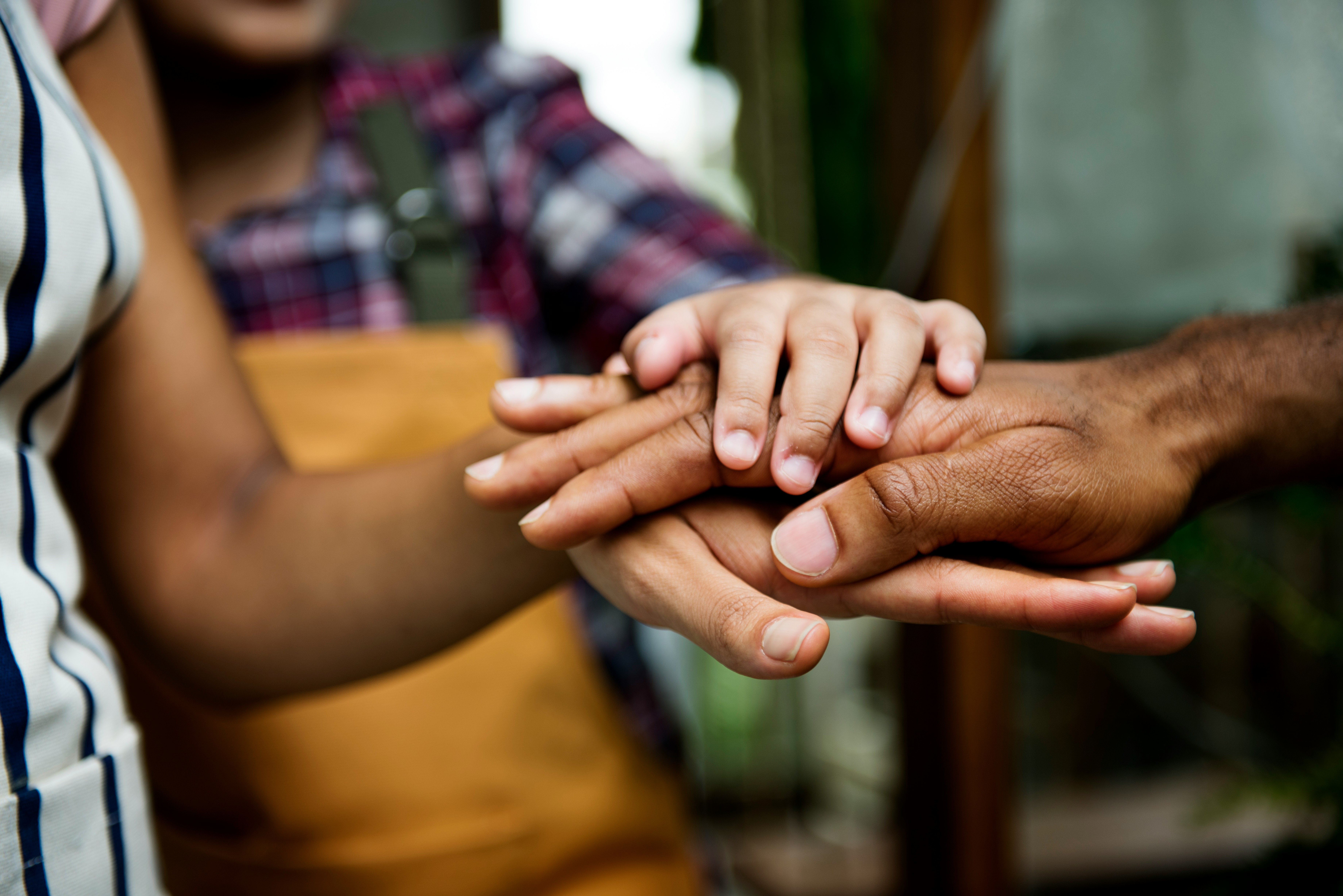 Close-up of diverse hands stacked in a supportive team gesture, symbolizing unity and mentorship in a collaborative work environment.